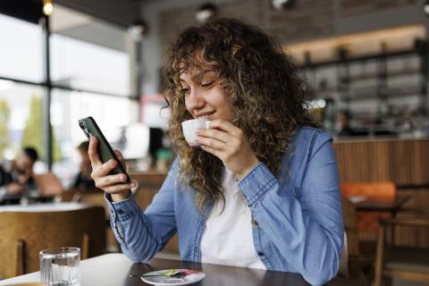 Femme qui regarde son téléphone en buvant un café